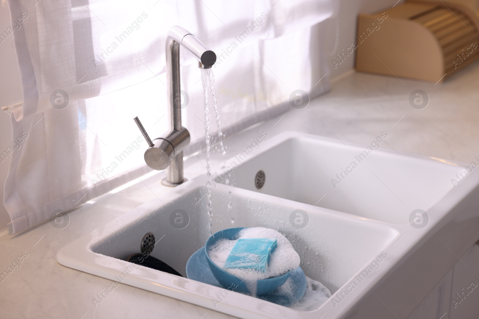 Photo of Dishes, blue sponge and foam under tap water in kitchen sink