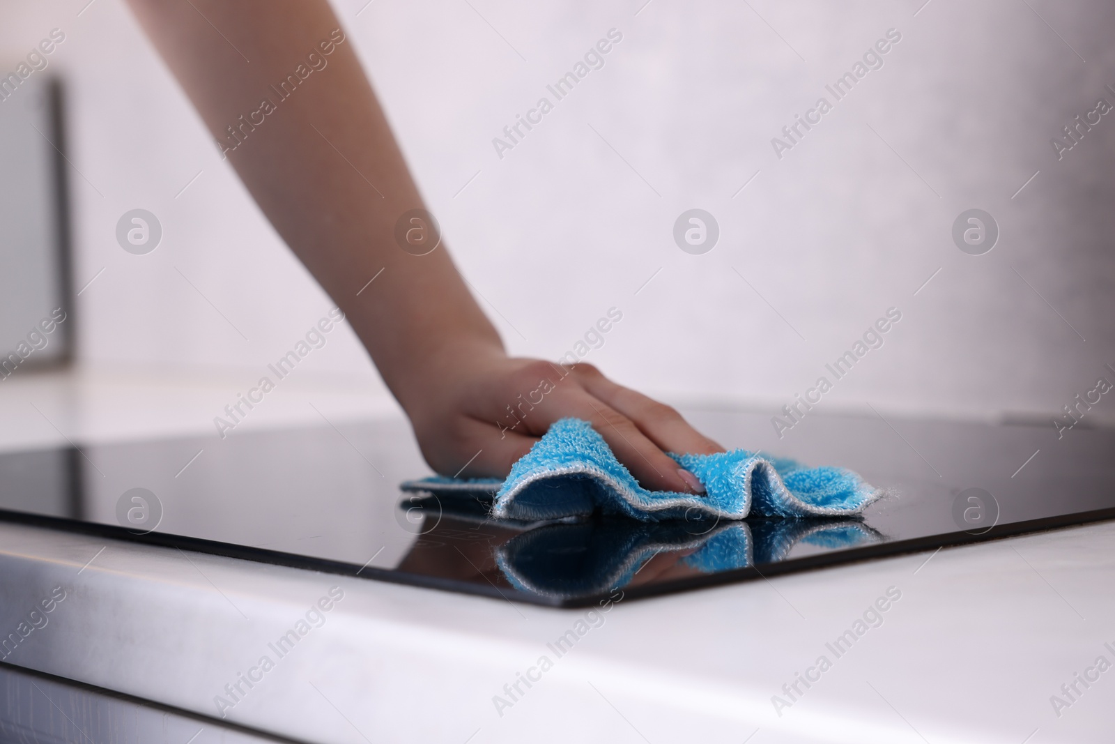 Photo of Woman cleaning induction cooktop with rag indoors, closeup