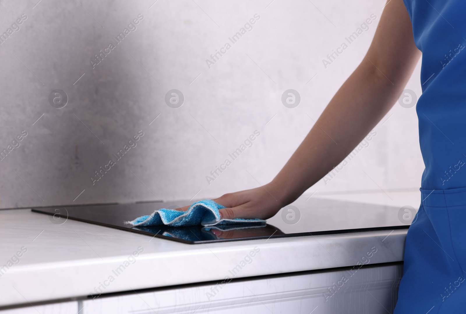 Photo of Woman cleaning induction cooktop with rag indoors, closeup