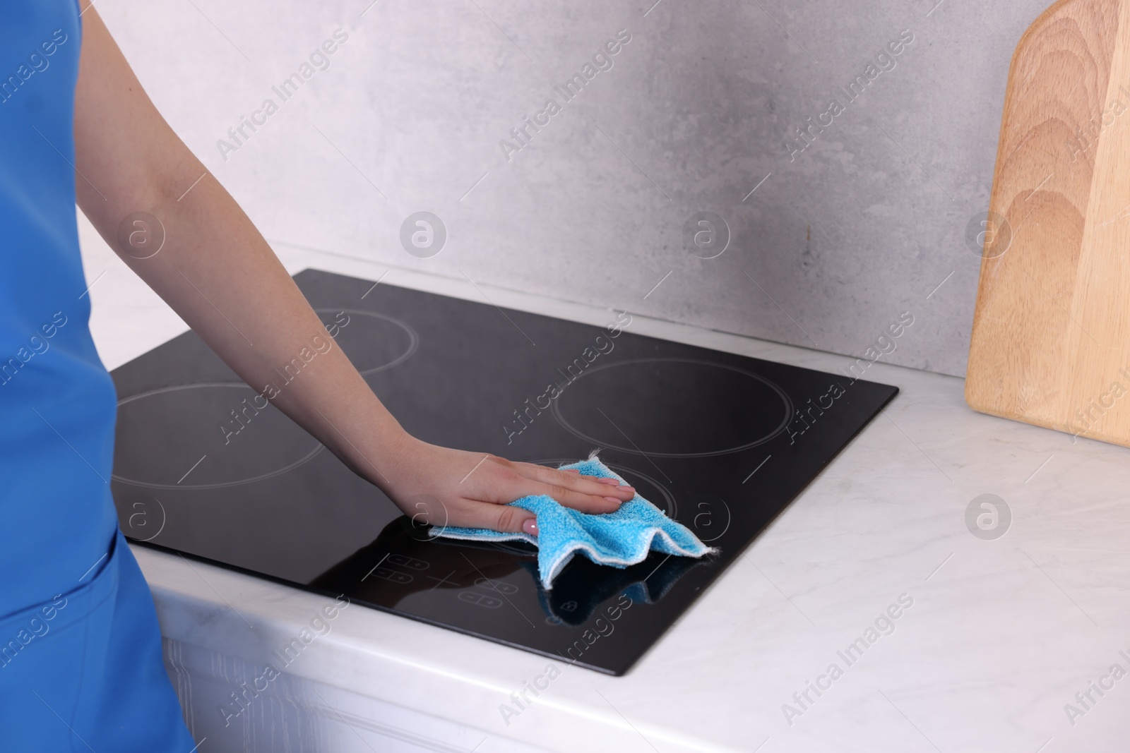 Photo of Woman cleaning induction cooktop with rag indoors, closeup