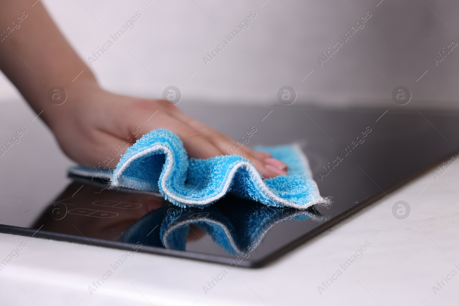 Photo of Woman cleaning induction cooktop with rag indoors, closeup