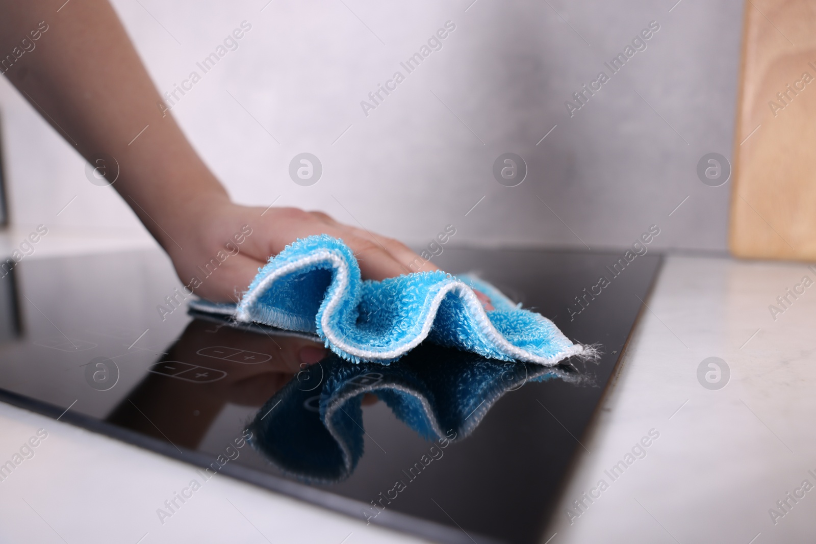 Photo of Woman cleaning induction cooktop with rag indoors, closeup