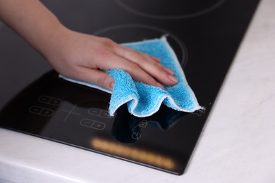 Photo of Woman cleaning induction cooktop with rag indoors, closeup