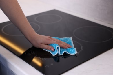 Photo of Woman cleaning induction cooktop with rag indoors, closeup