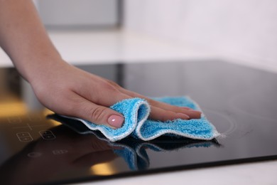 Photo of Woman cleaning induction cooktop with rag indoors, closeup