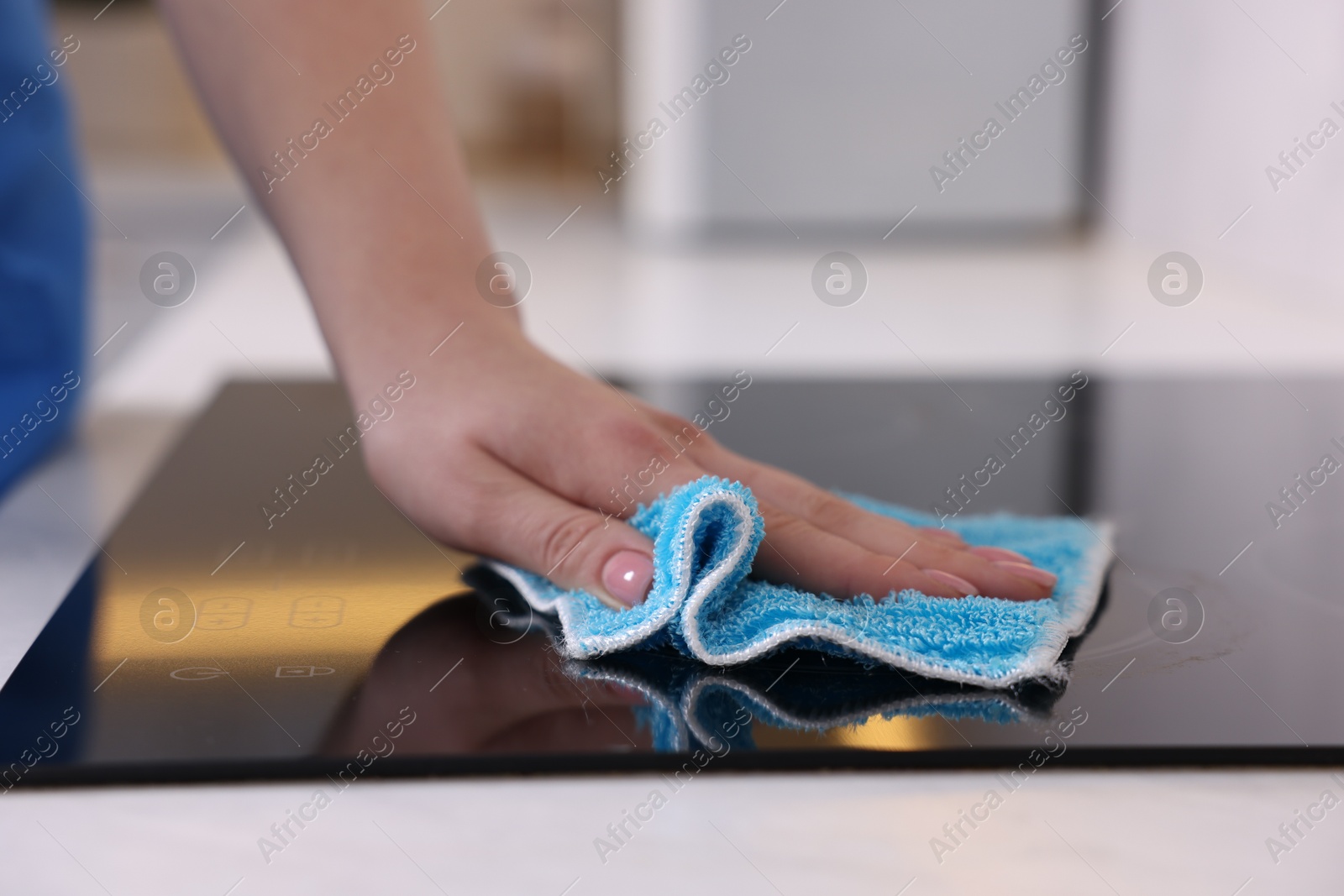 Photo of Woman cleaning induction cooktop with rag indoors, closeup