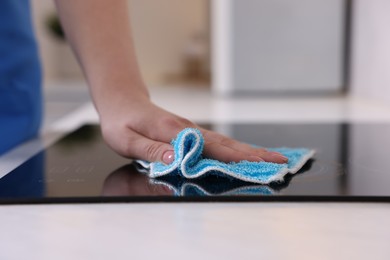 Photo of Woman cleaning induction cooktop with rag indoors, closeup