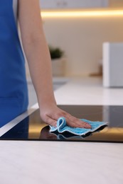 Photo of Woman cleaning induction cooktop with rag indoors, closeup