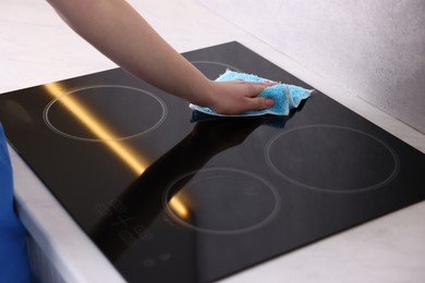 Photo of Woman cleaning induction cooktop with rag indoors, closeup