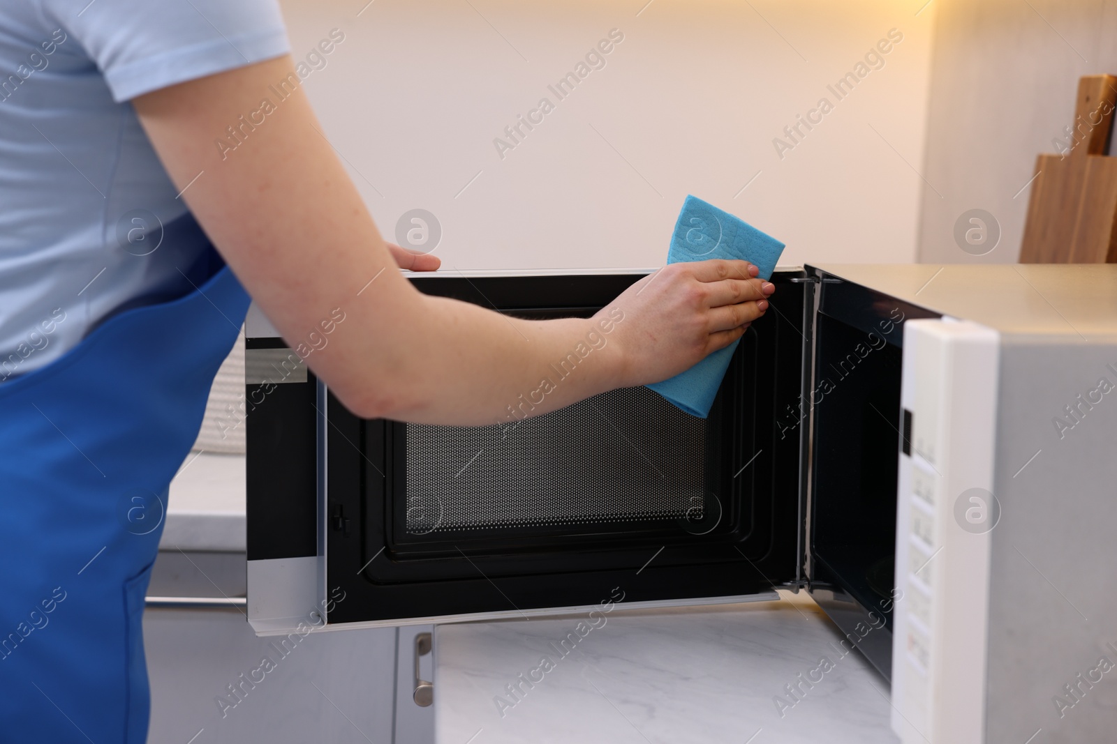 Photo of Woman cleaning microwave oven with rag indoors, closeup