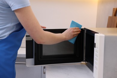 Photo of Woman cleaning microwave oven with rag indoors, closeup