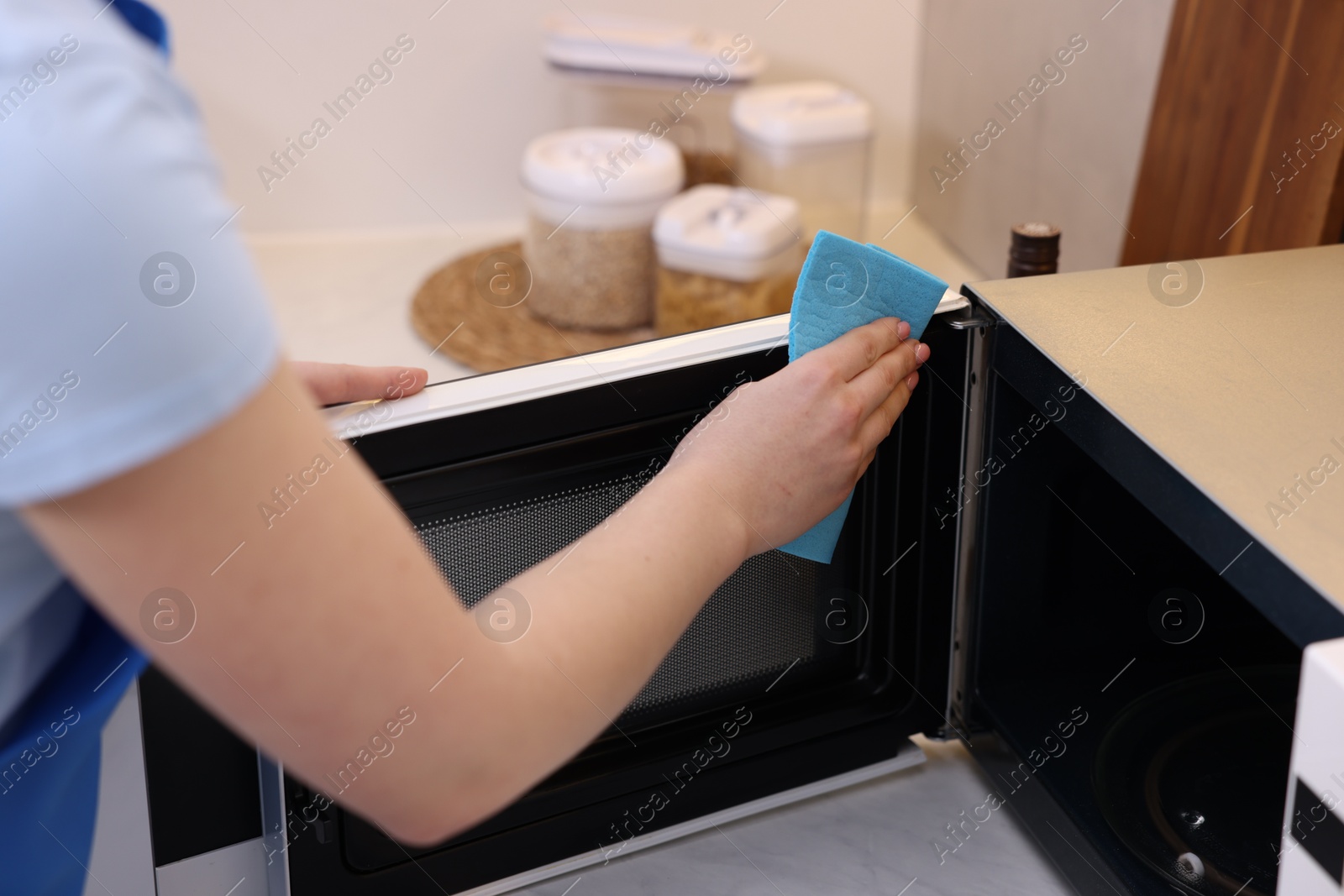 Photo of Woman cleaning microwave oven with rag indoors, closeup