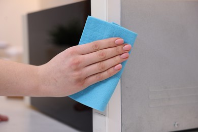 Photo of Woman cleaning microwave oven with rag indoors, closeup