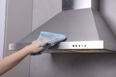 Photo of Woman cleaning kitchen hood with rag indoors, closeup