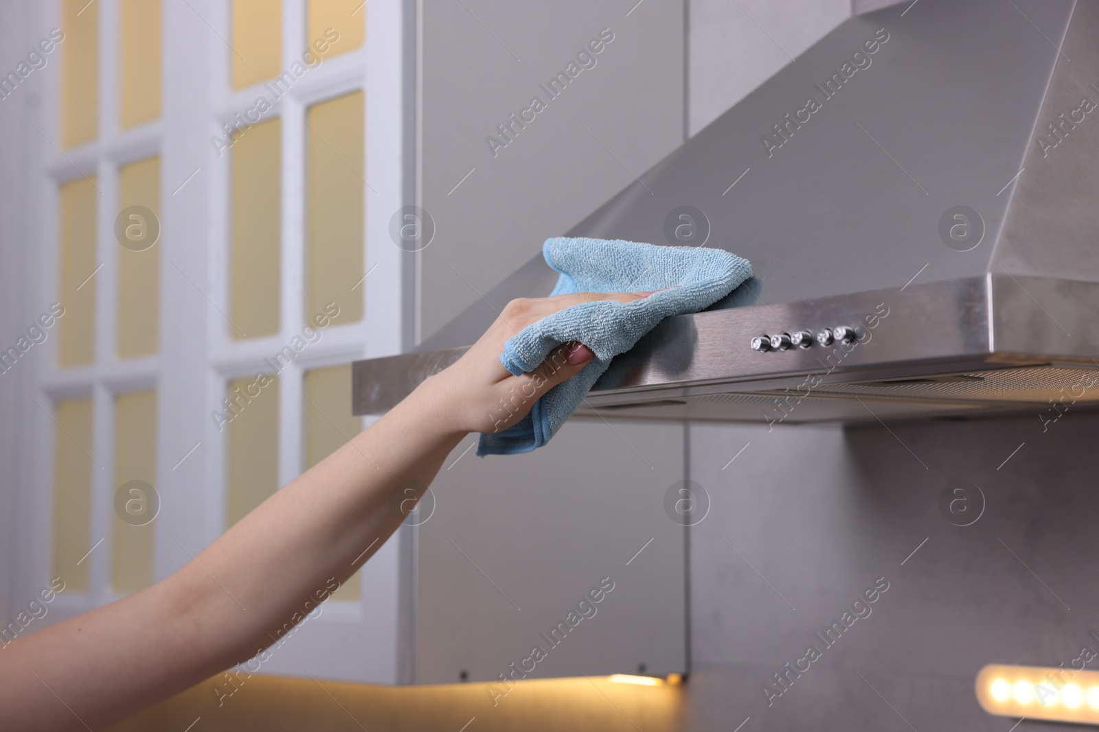 Photo of Woman cleaning kitchen hood with rag indoors, closeup