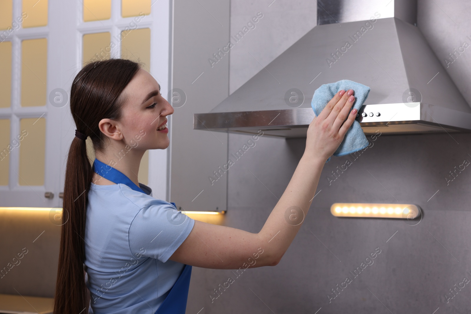 Photo of Smiling woman cleaning kitchen hood with rag indoors