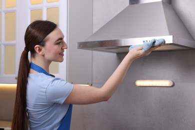 Photo of Smiling woman cleaning kitchen hood with rag indoors