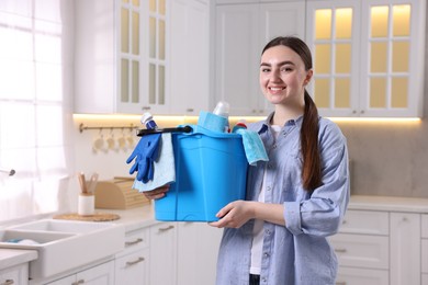 Photo of Smiling woman holding bucket with cleaning supplies in kitchen