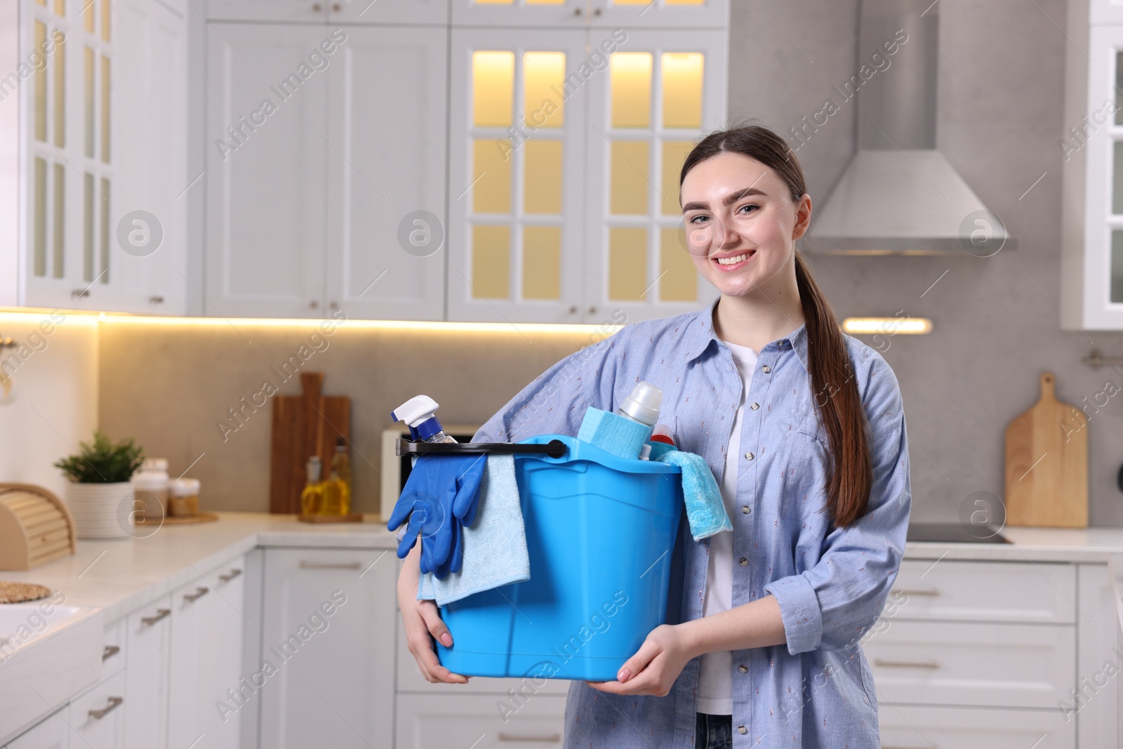 Photo of Smiling woman holding bucket with cleaning supplies in kitchen