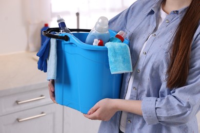 Photo of Woman holding bucket with cleaning supplies in kitchen, closeup