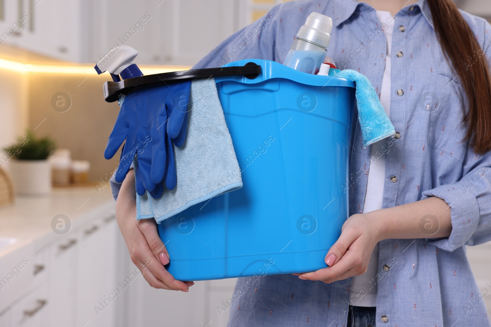 Photo of Woman holding bucket with cleaning supplies in kitchen, closeup