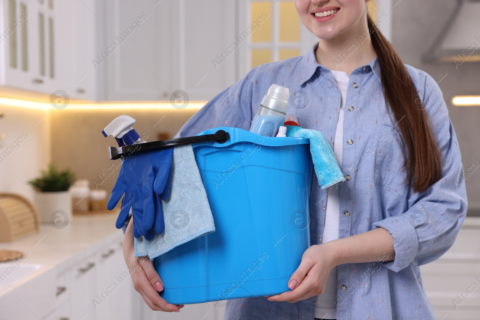 Photo of Woman holding bucket with cleaning supplies in kitchen, closeup