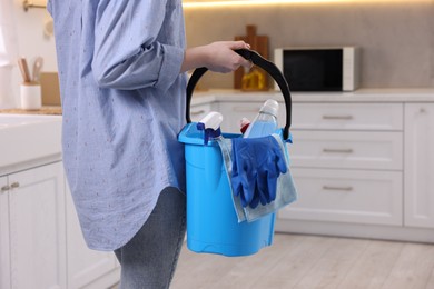 Photo of Woman holding bucket with cleaning supplies in kitchen, closeup