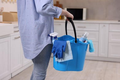 Photo of Woman holding bucket with cleaning supplies in kitchen, closeup