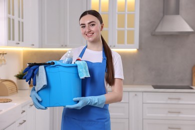 Photo of Smiling woman holding bucket with cleaning supplies in kitchen