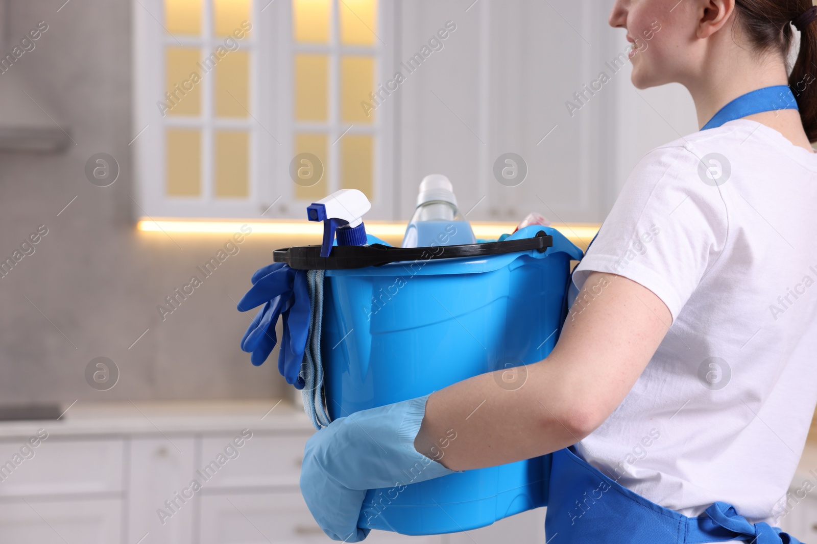 Photo of Woman with bucket with cleaning supplies in kitchen, closeup