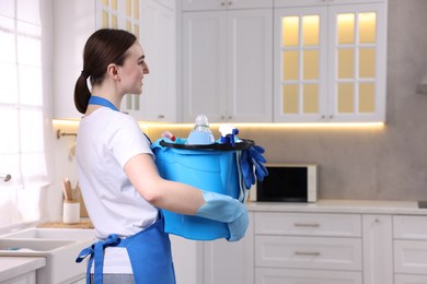 Photo of Smiling woman holding bucket with cleaning supplies in kitchen