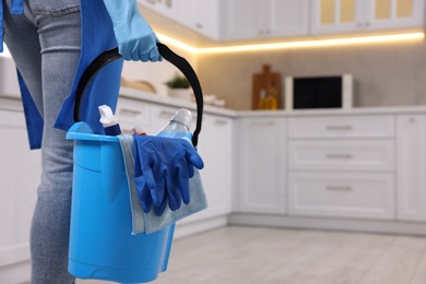 Photo of Woman with bucket with cleaning supplies in kitchen, closeup