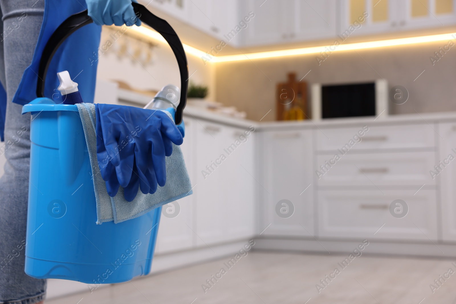 Photo of Woman with bucket with cleaning supplies in kitchen, closeup