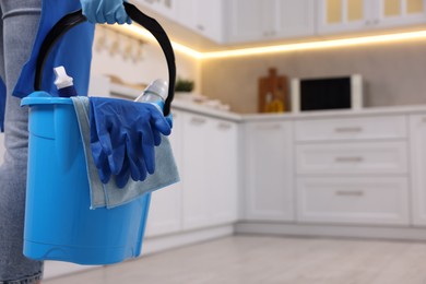 Photo of Woman with bucket with cleaning supplies in kitchen, closeup