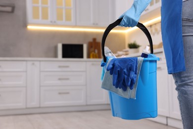 Photo of Woman with bucket with cleaning supplies in kitchen, closeup