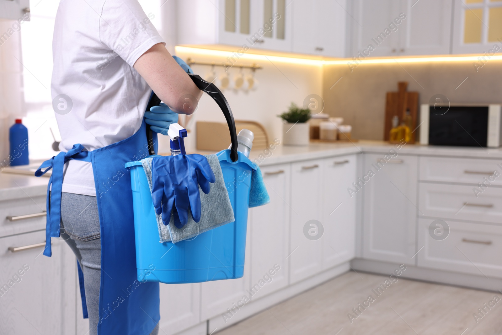 Photo of Woman holding bucket with cleaning supplies in kitchen, closeup