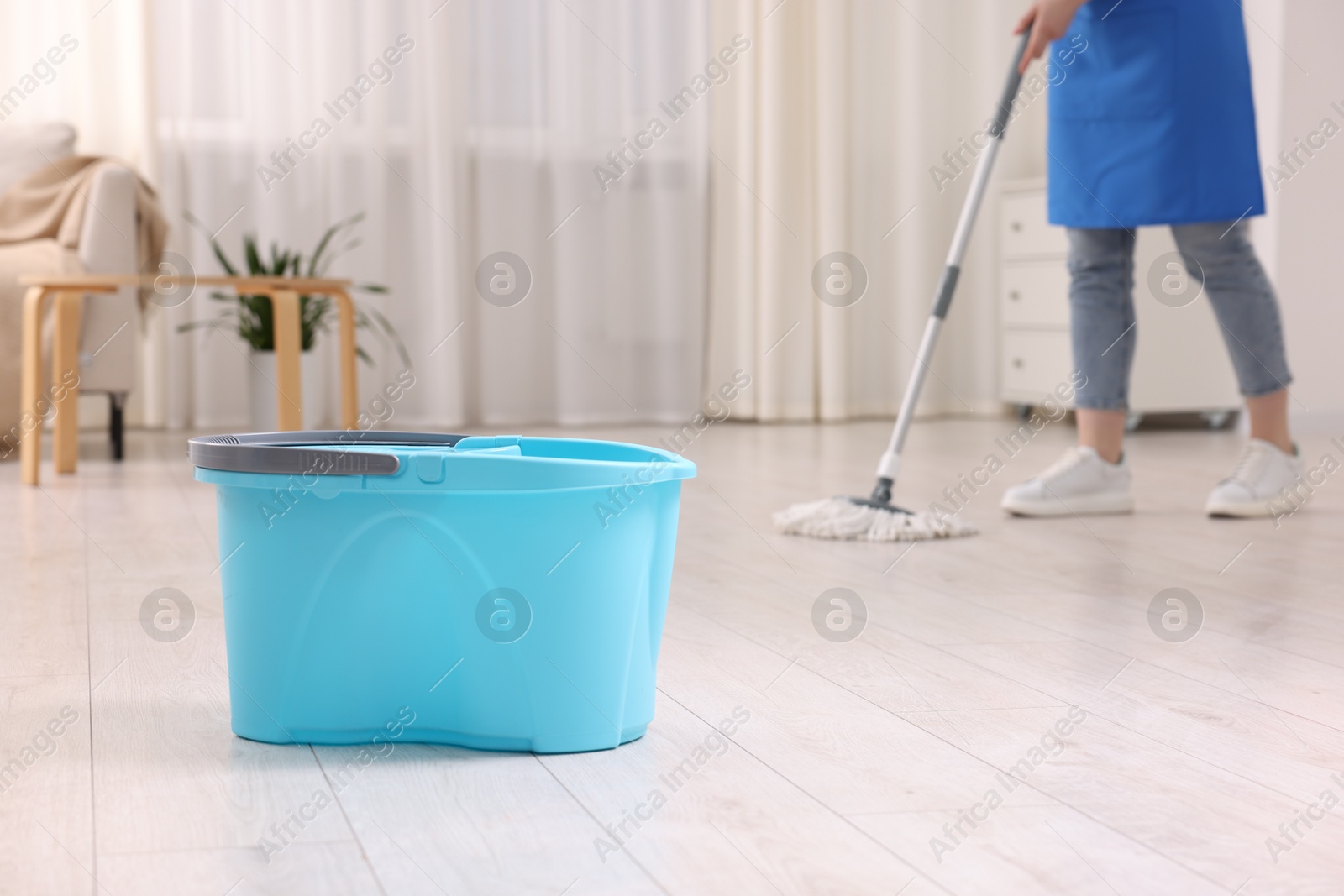 Photo of Woman cleaning floor with string mop indoors, focus on bucket