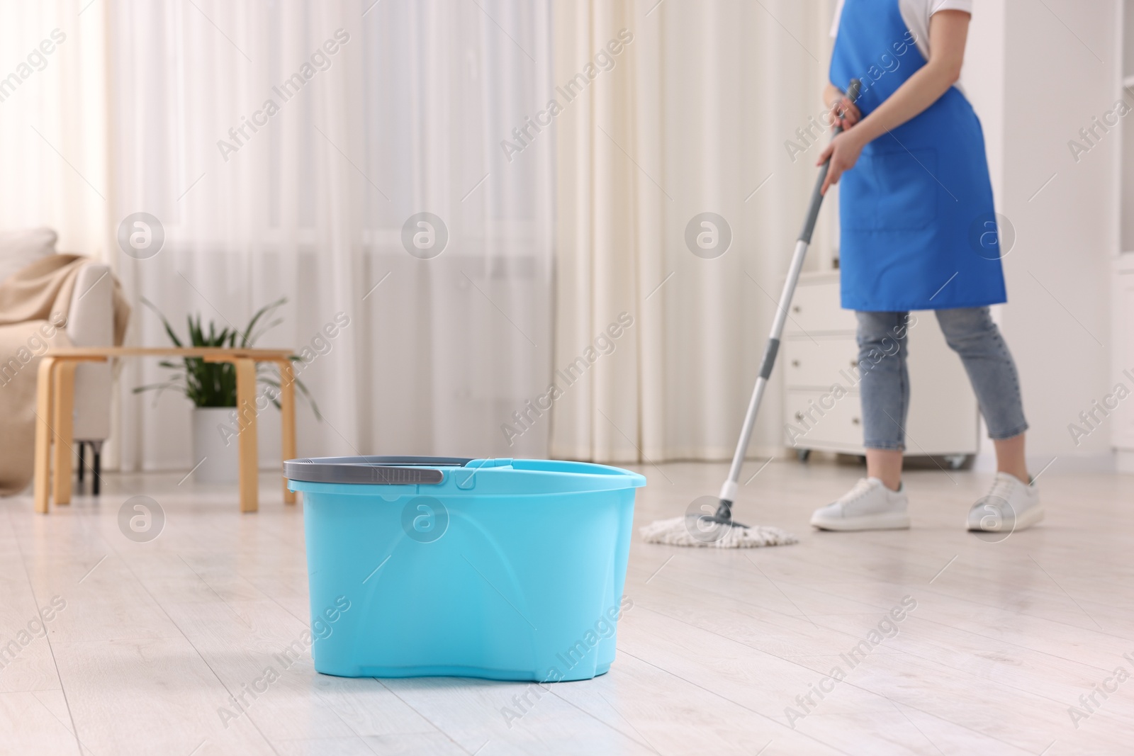 Photo of Woman cleaning floor with string mop indoors, focus on bucket