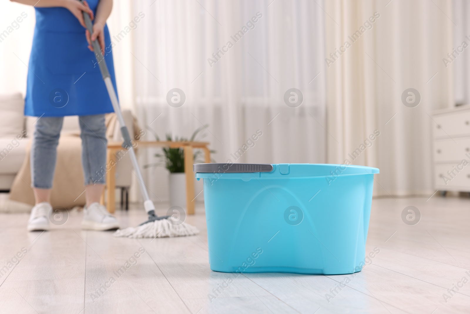 Photo of Woman cleaning floor with string mop indoors, focus on bucket