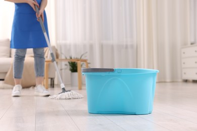 Photo of Woman cleaning floor with string mop indoors, focus on bucket