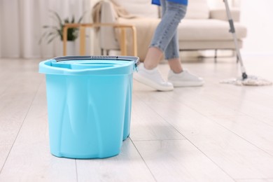 Photo of Woman cleaning floor with string mop indoors, focus on bucket