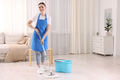 Photo of Smiling woman cleaning floor with string mop indoors