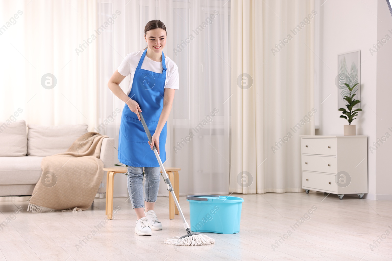 Photo of Smiling woman cleaning floor with string mop indoors