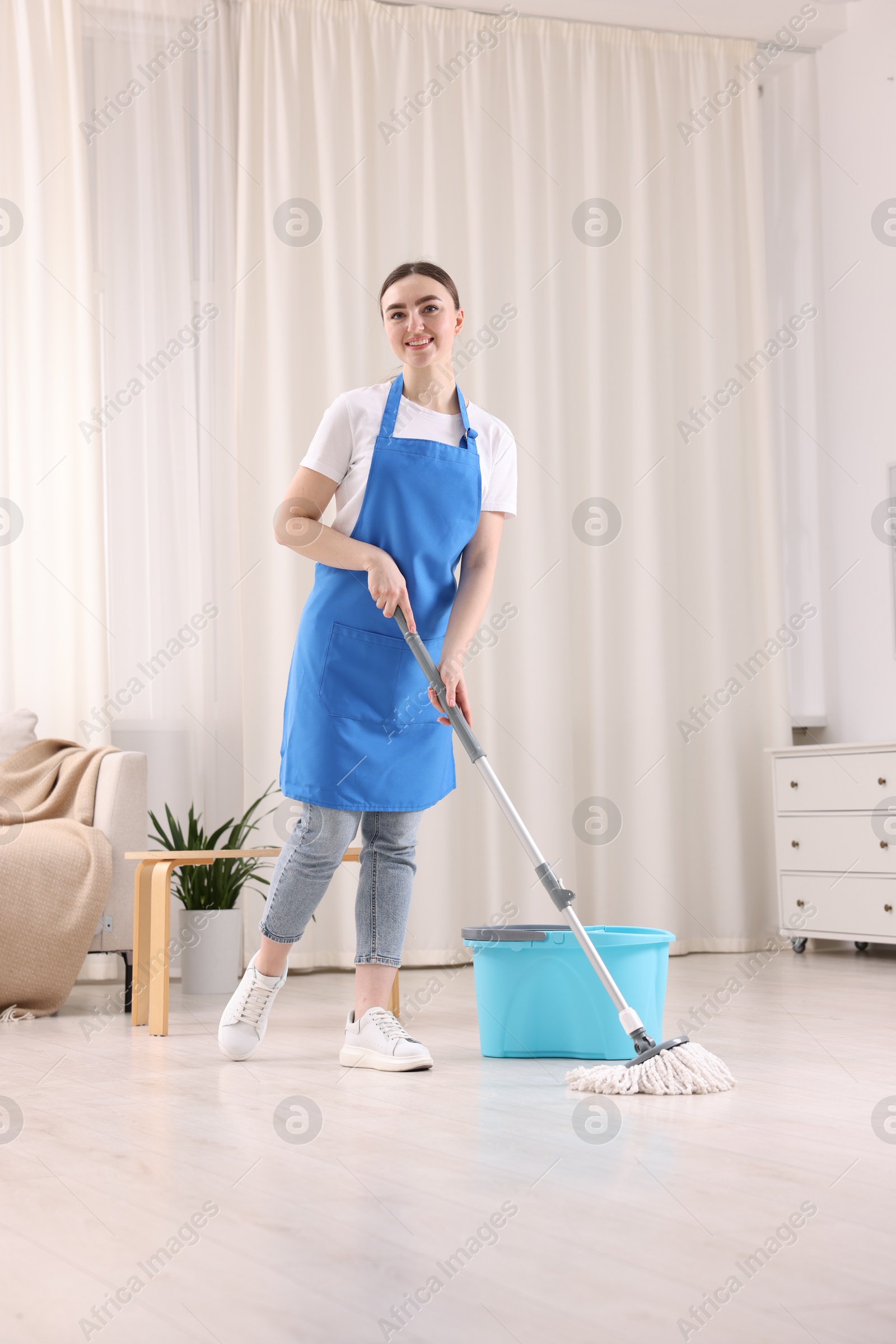 Photo of Smiling woman cleaning floor with string mop indoors