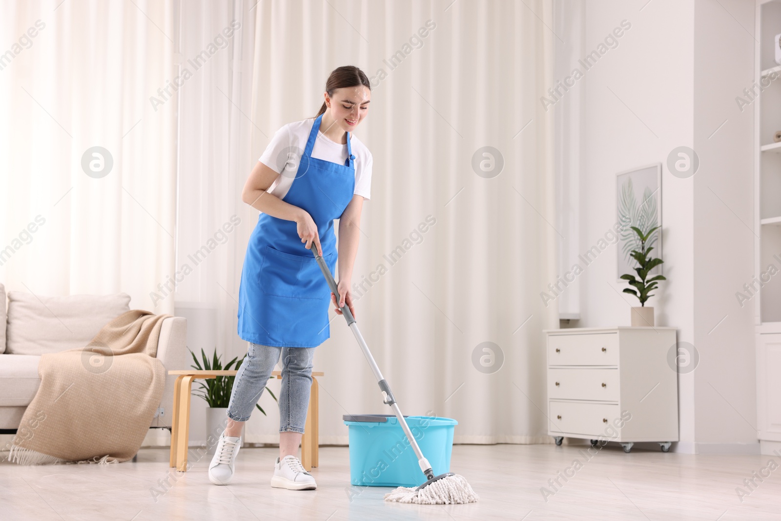 Photo of Smiling woman cleaning floor with string mop indoors