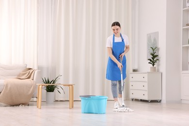 Photo of Smiling woman cleaning floor with string mop indoors