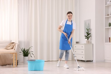 Photo of Smiling woman cleaning floor with string mop indoors