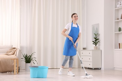 Photo of Smiling woman cleaning floor with string mop indoors