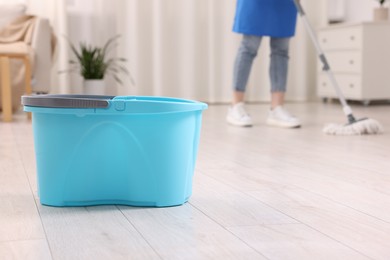 Photo of Woman cleaning floor with string mop indoors, focus on bucket