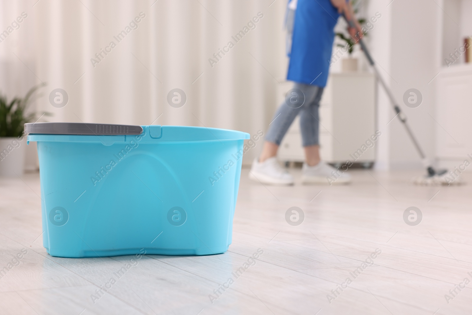 Photo of Woman cleaning floor with string mop indoors, focus on bucket